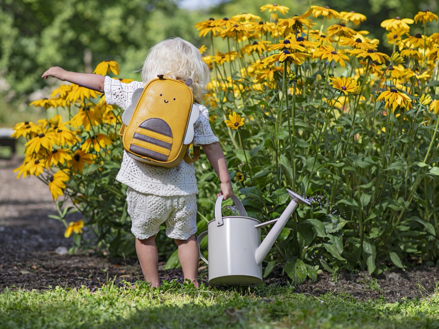 A child with a Drömpals bee backpack watering sunflowers