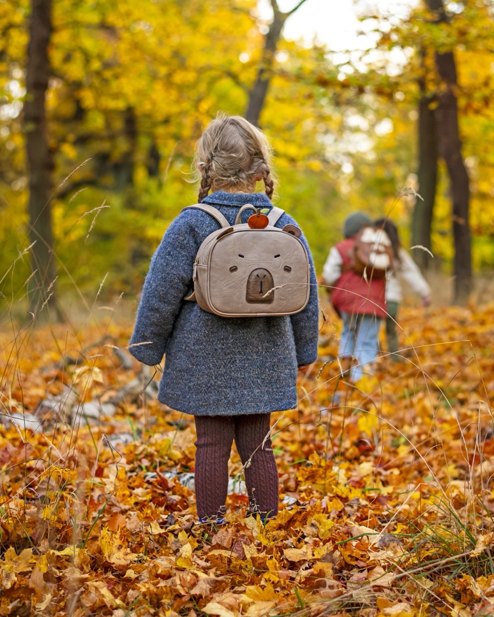 A child wearing a Drömpals capybara backpack in an autumn forest